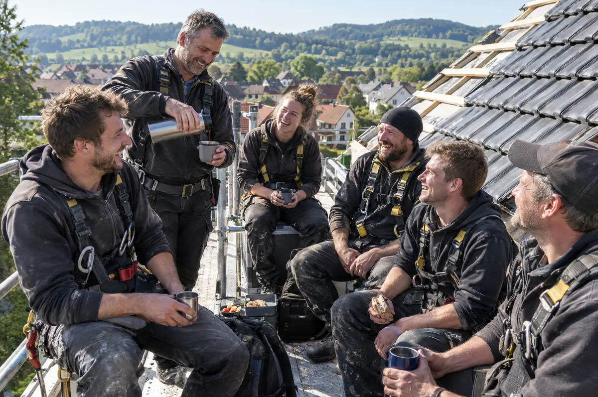 Team einer Dachdeckerei bei der Kaffeepause auf dem Dach